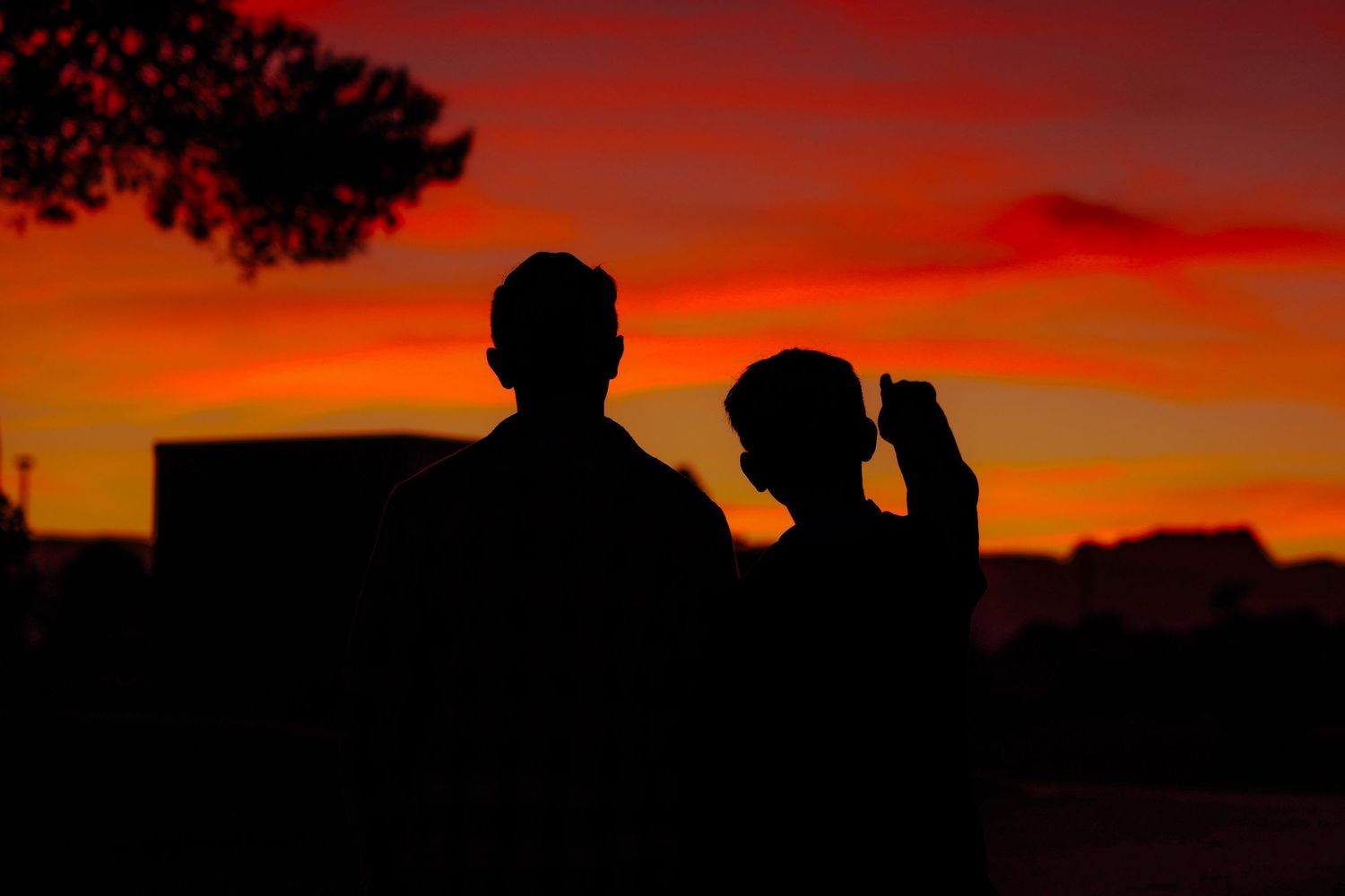 Romantic silhouette of couple against vibrant red and orange sunset sky at dusk.