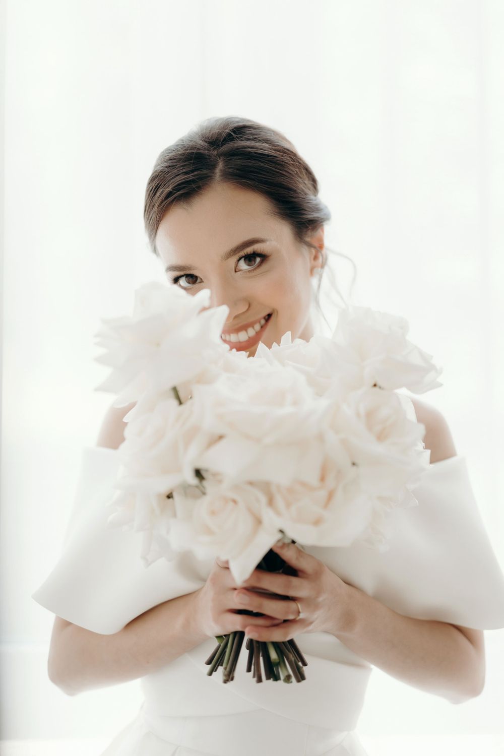 Bride smiling and looking through white flowers arranged in a bridal bouquet