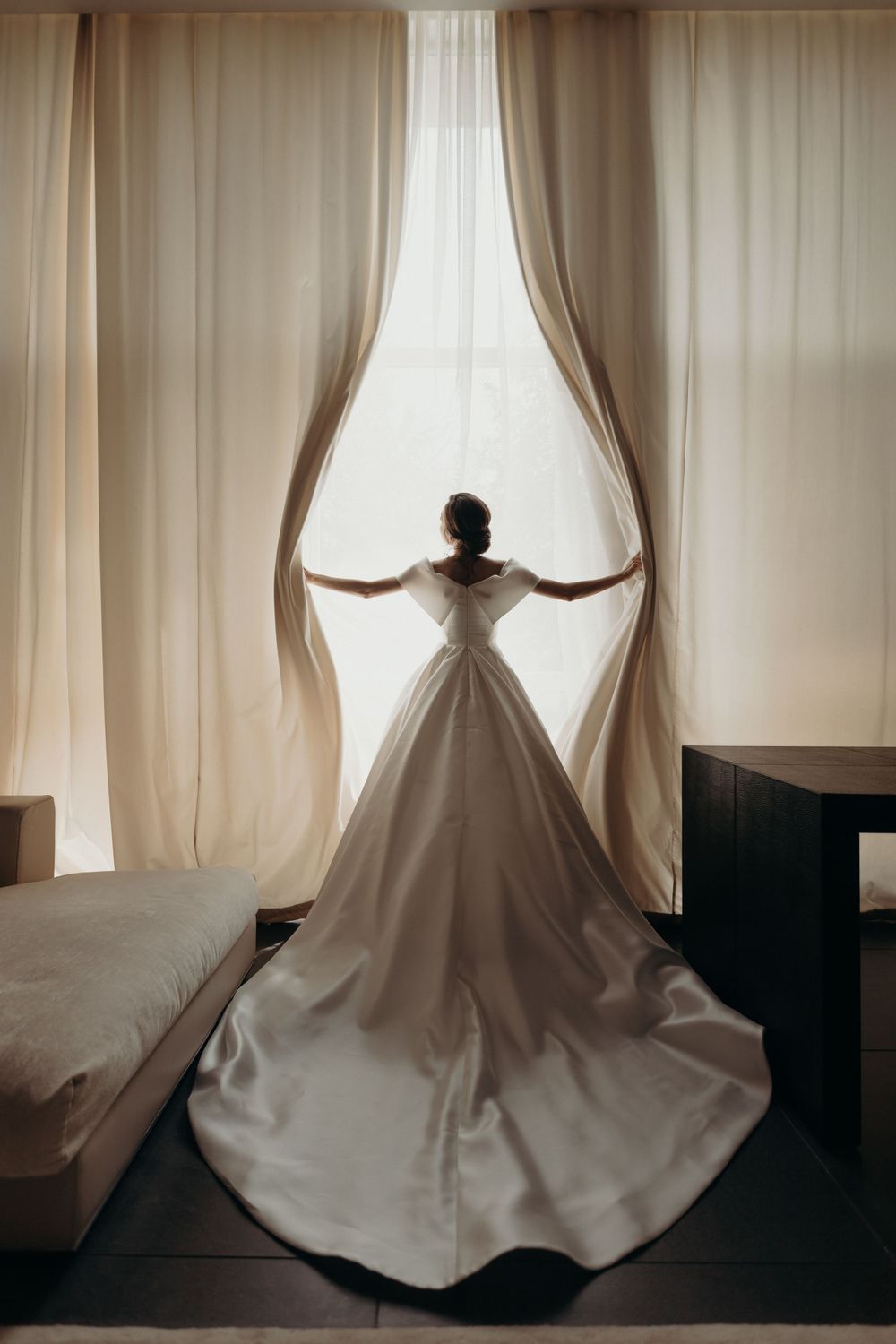 Bride wearing long white dress standing by the window