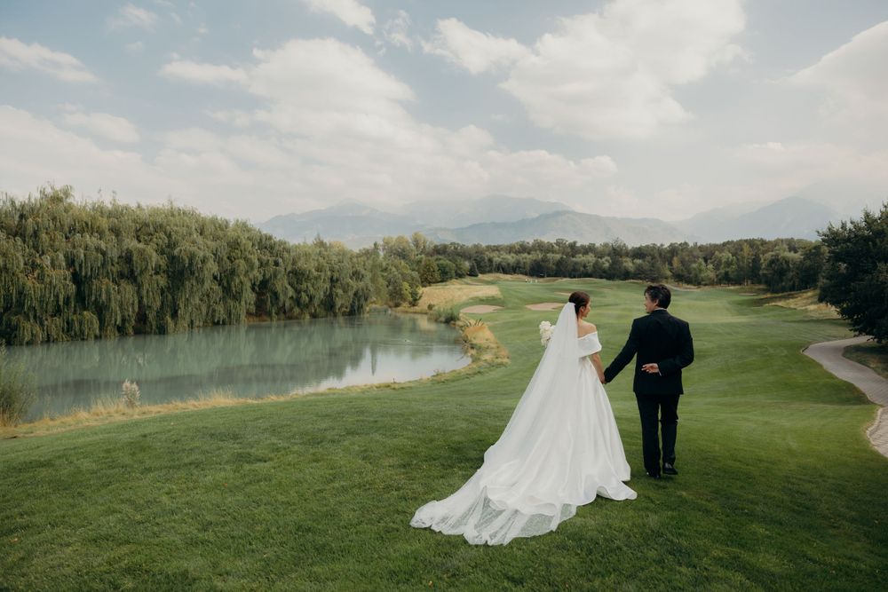 Bride and groom walking in a green field by the pond with mountains in the background