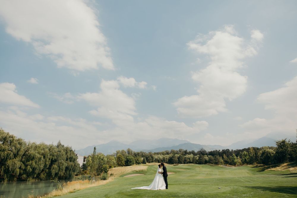 Couple in wedding attire standing in a green field in the distance