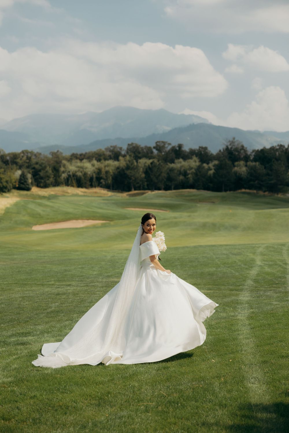 Woman in a long white wedding dress standing in a green field and smiling