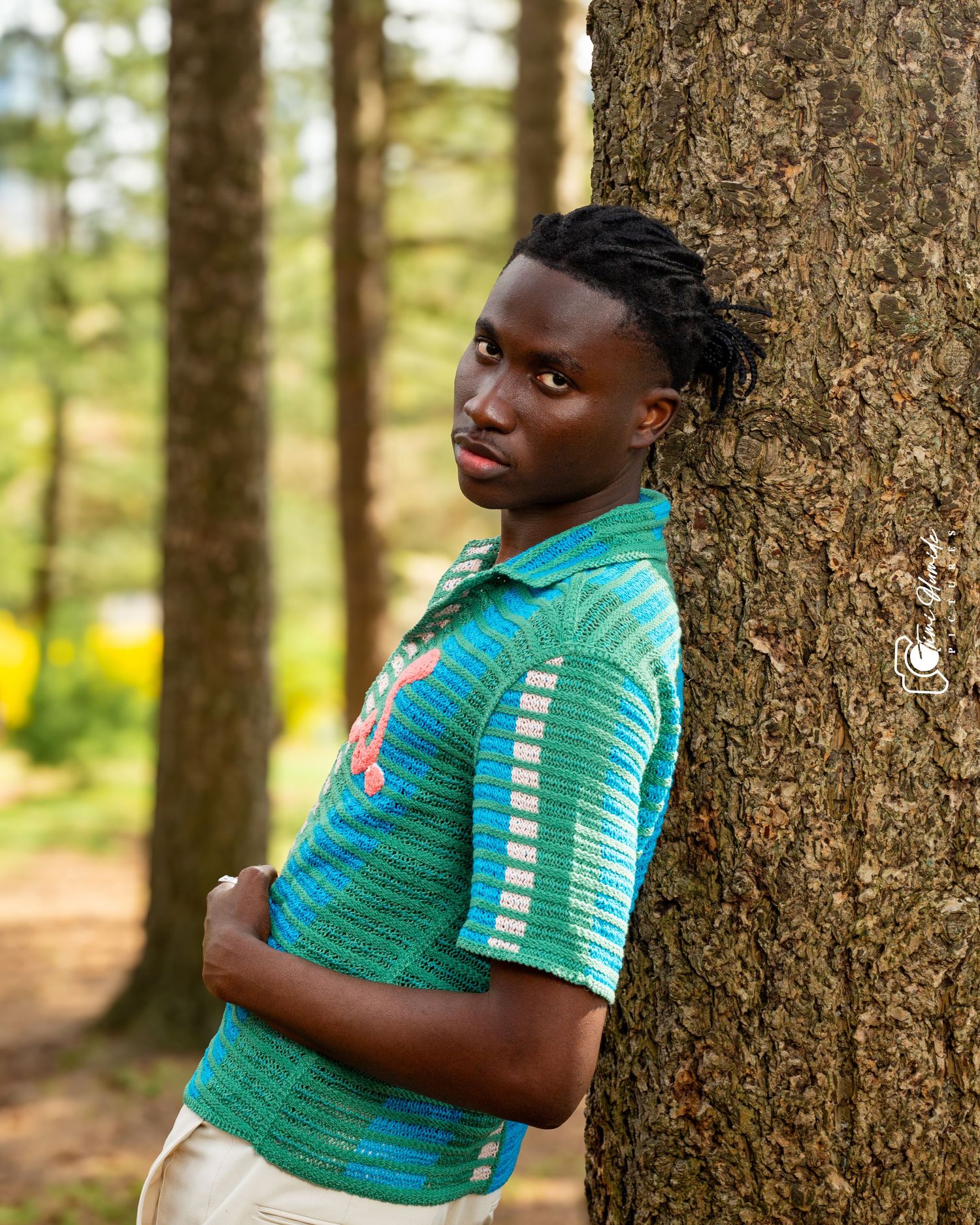 Portrait of person in turquoise polo shirt leaning against tree trunk in sunny forest.