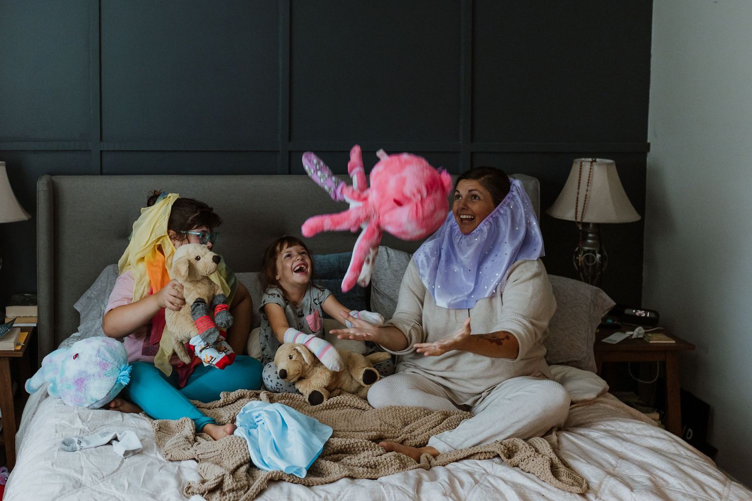 A mother and daughters playing with stuffed animals on bed. Whitney Popp, Arizona photographer.