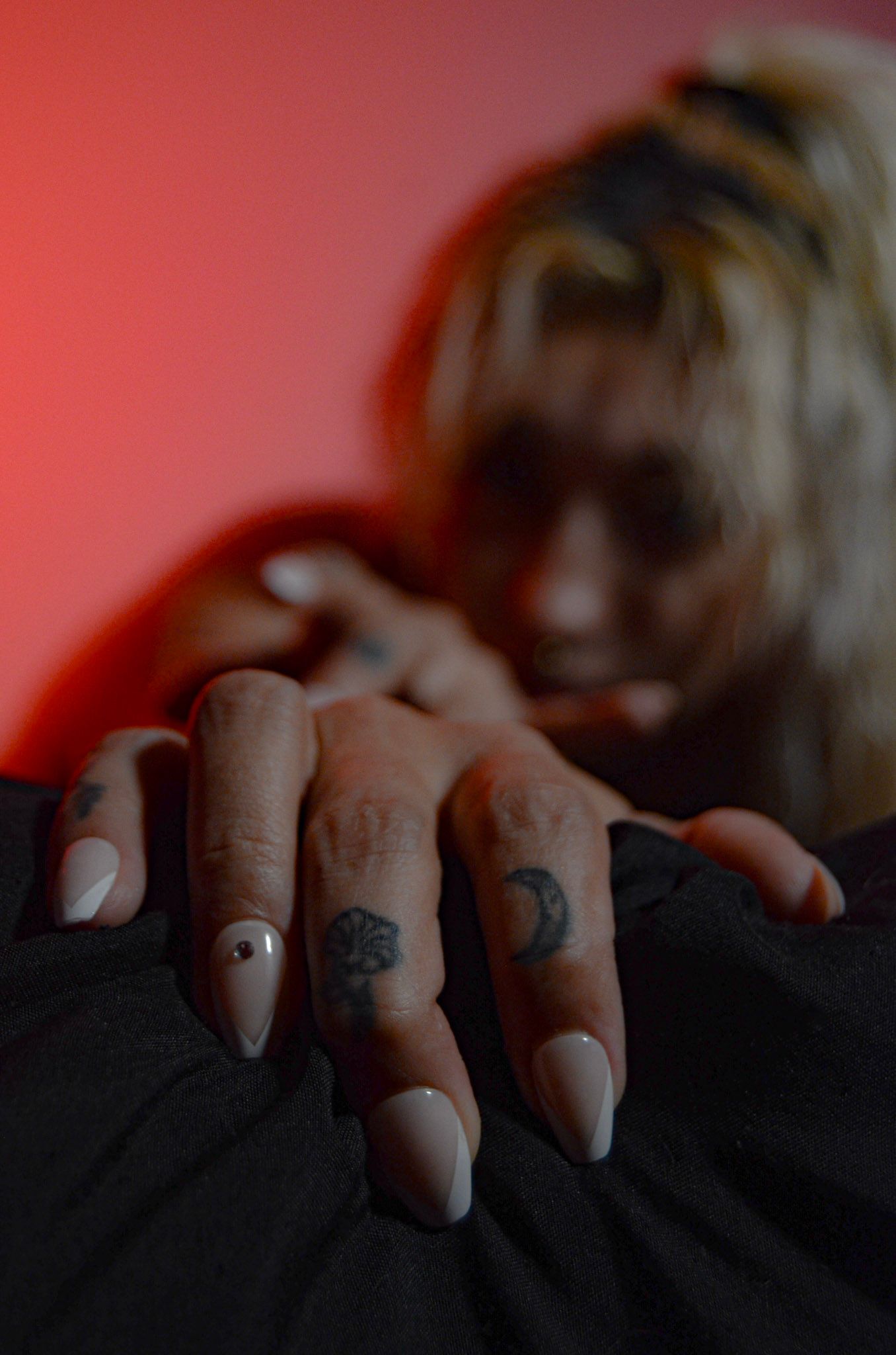 Close-up of manicured fingers with tattoos gripping dark fabric.