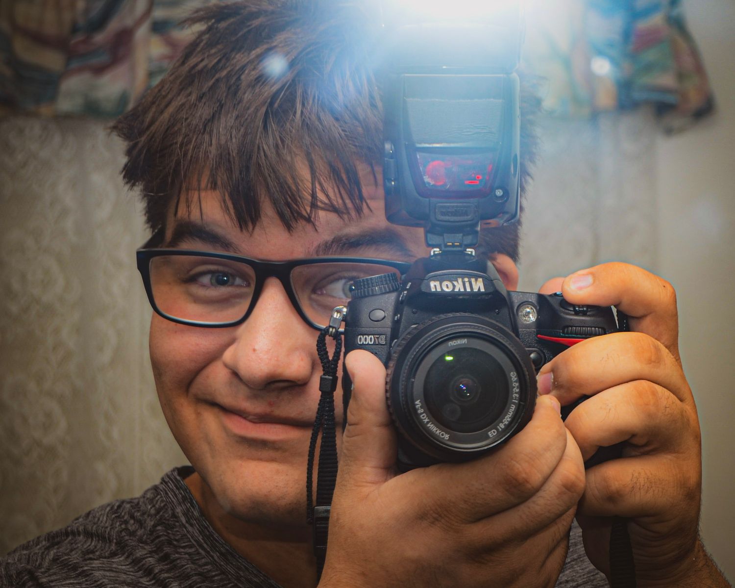 Self portrait reflection showing someone holding a Nikon camera with flash attachment.