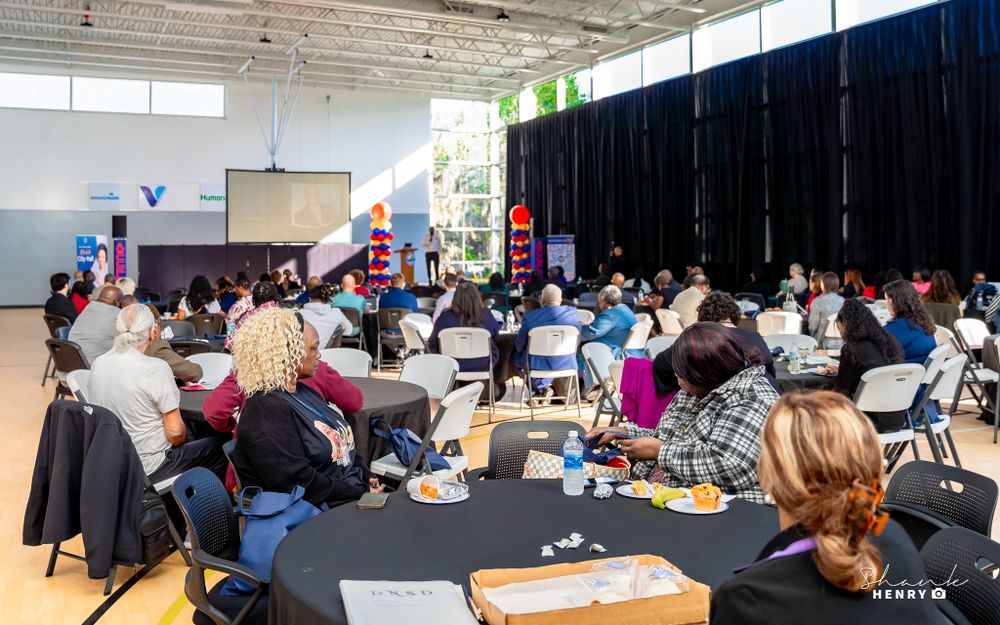 Audience members seated at round tables in a large hall during an event.
