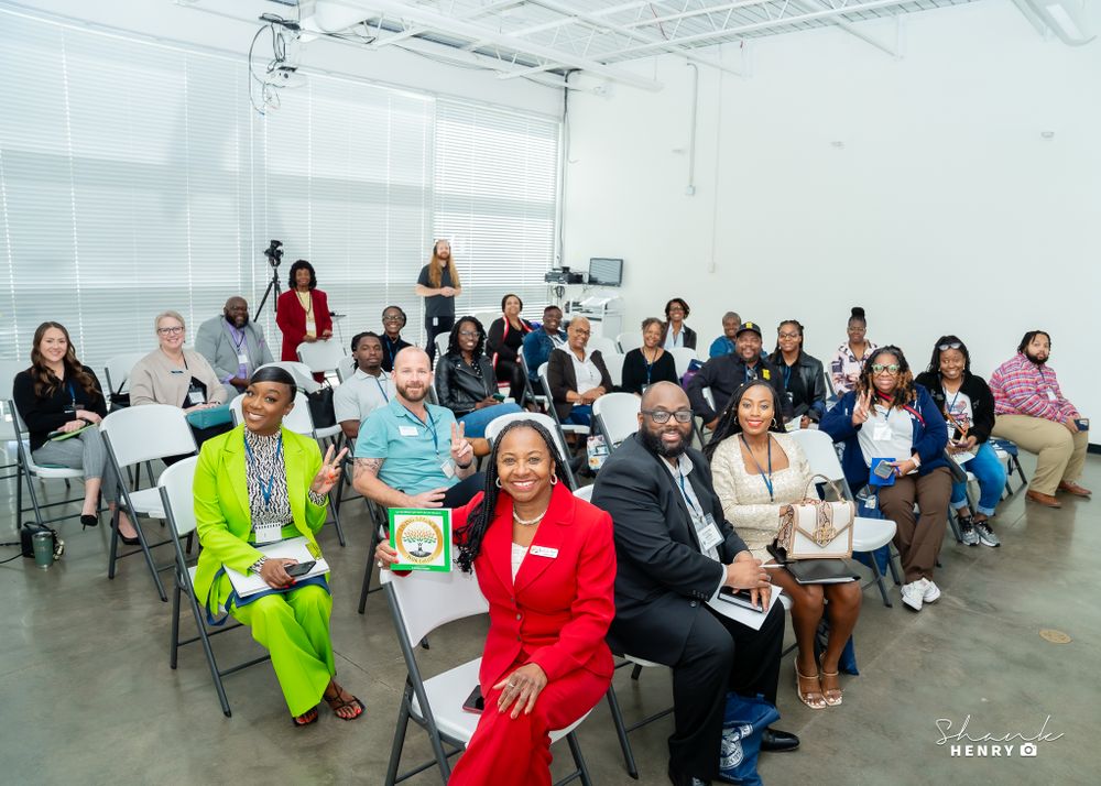 Large group of attendees seated in chairs during an indoor event in a bright white room.