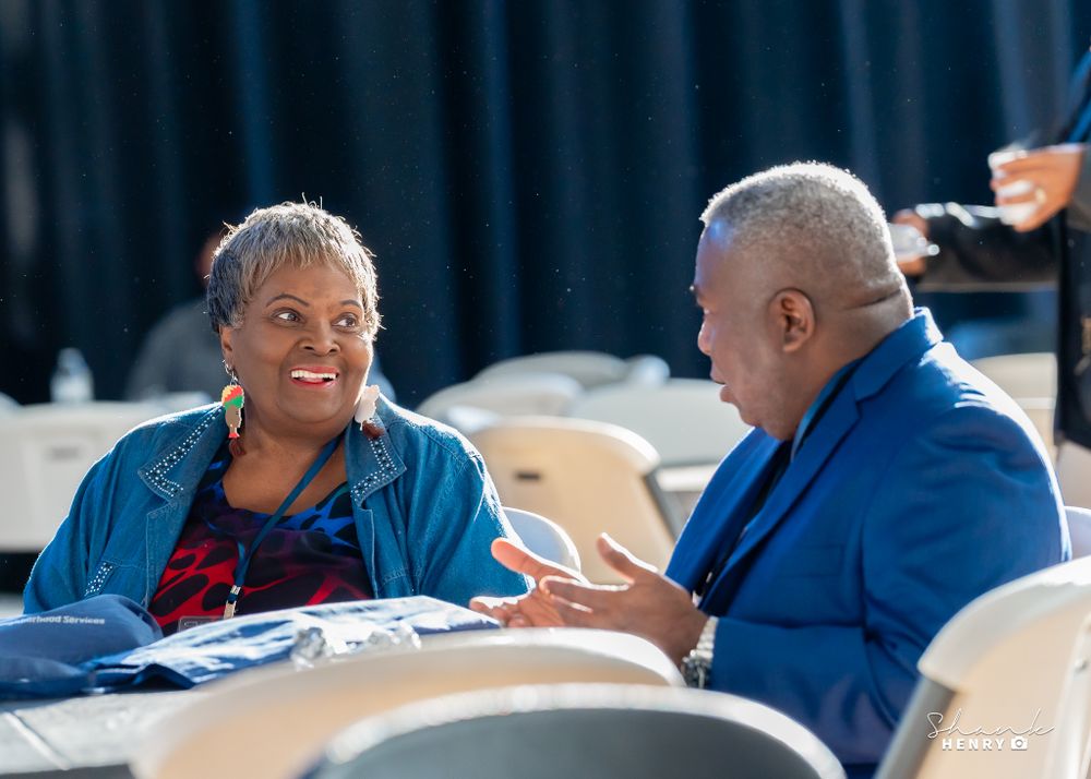 Two colleagues having an animated discussion while seated at round tables during a meeting.