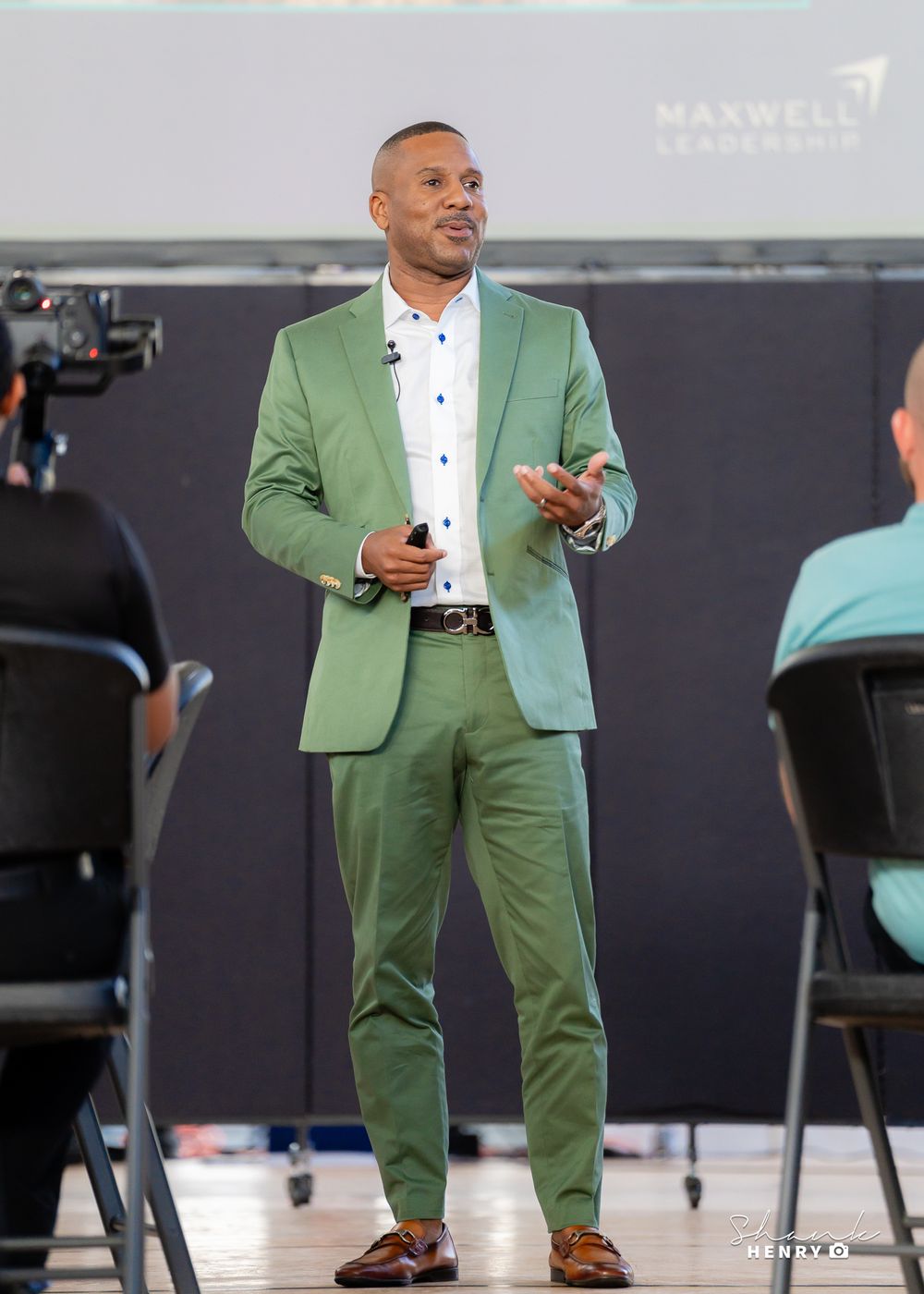 Speaker in mint green suit presenting on stage at corporate event.