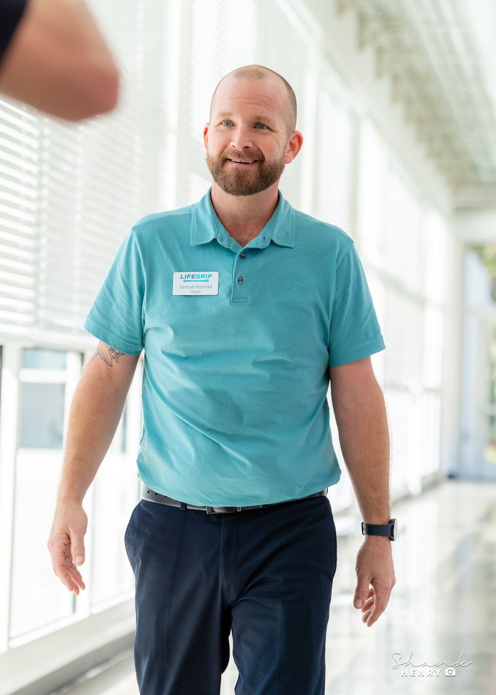 Staff member in turquoise polo shirt walking through bright corridor.