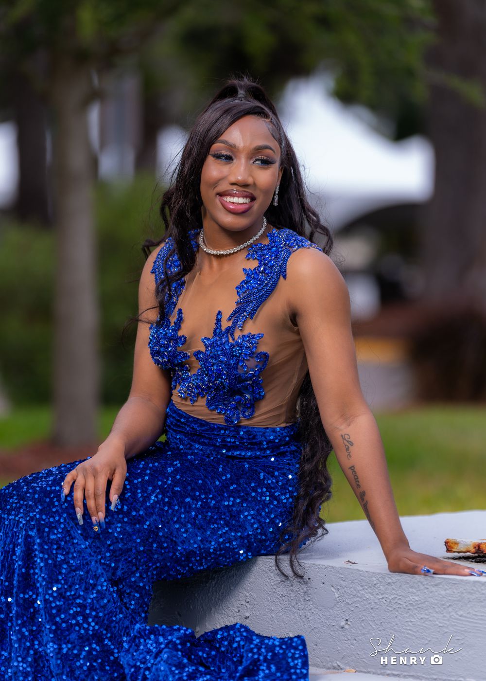 A woman in a royal blue sequined gown poses elegantly on a concrete surface outdoors.