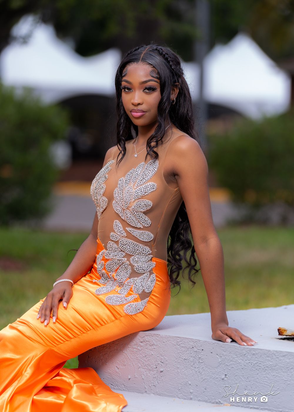 A woman in an orange and silver form-fitting gown poses gracefully against a light-colored wall.