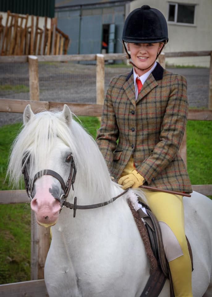 A rider in formal equestrian attire sits atop a white pony with traditional tack.