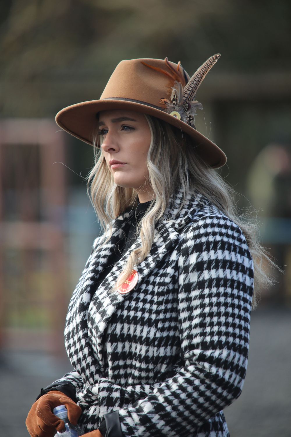 An elegant equestrian style portrait featuring houndstooth coat and feathered tan hat.