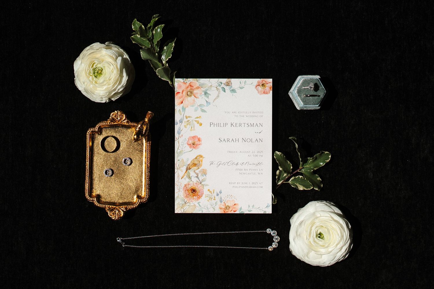 Wedding rings and earrings displayed in hexagonal velvet boxes with a white rose.