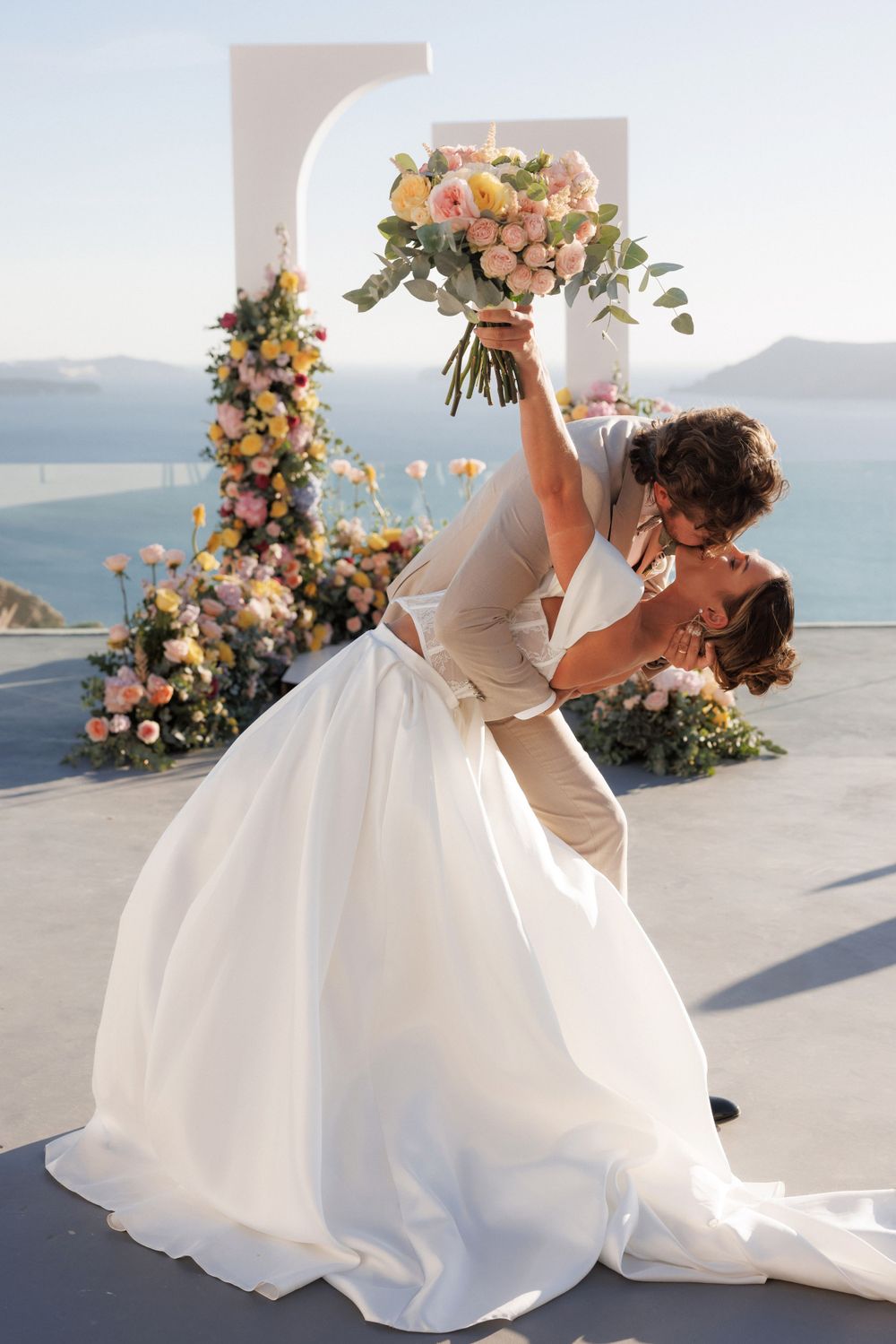 A romantic dip dance pose during a seaside wedding with floral decorations and ocean views.