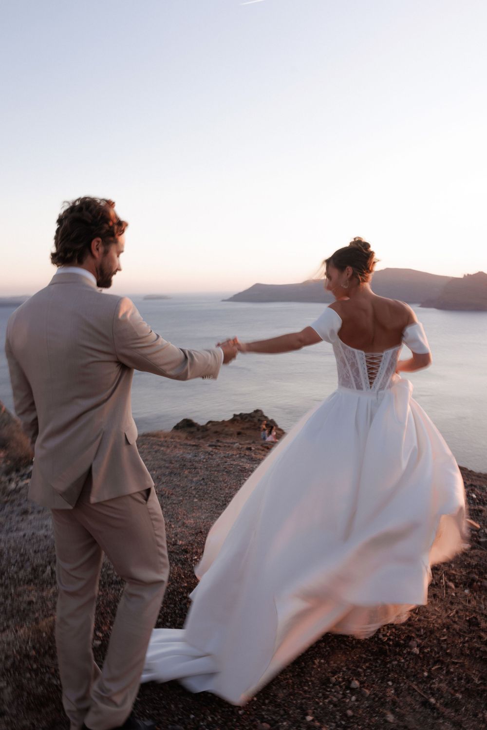 A bride and groom dance together at sunset on a cliffside overlooking the Mediterranean Sea.