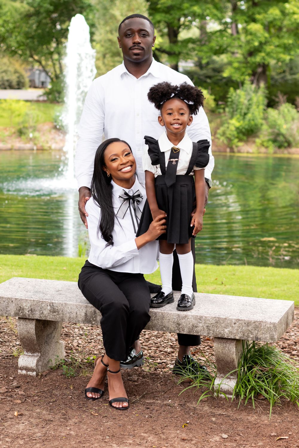 A joyful Black family poses near a fountain in a park, wearing matching black and white outfits.