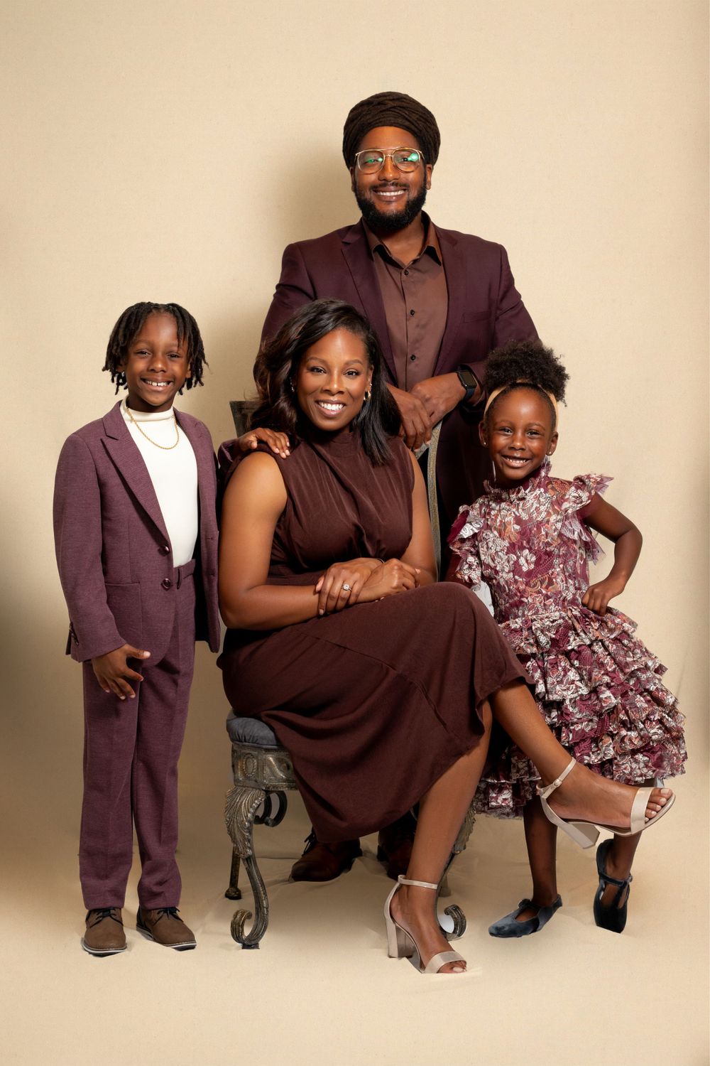A family wearing coordinated burgundy outfits poses together for a formal portrait against a beige backdrop.