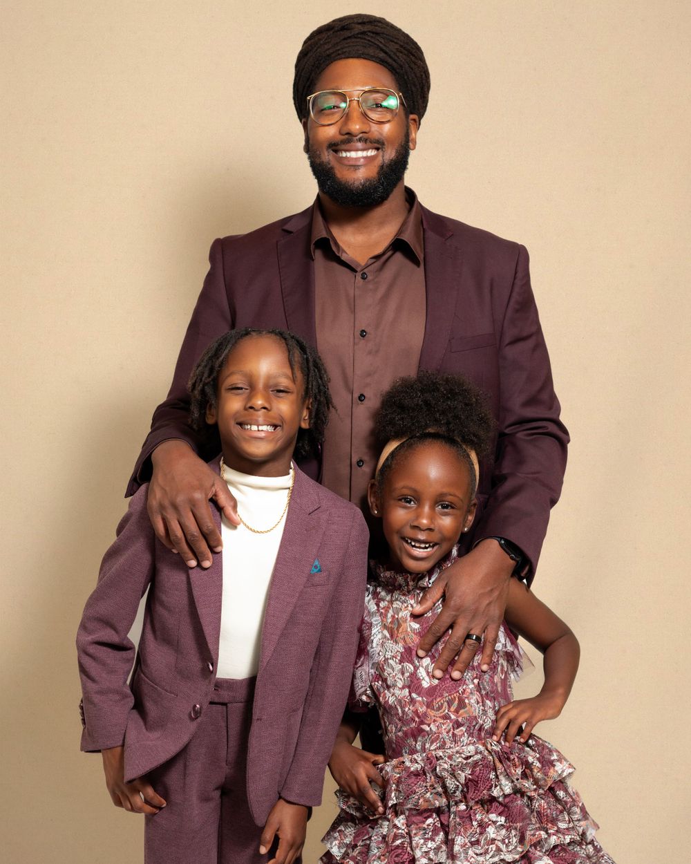 A group wearing coordinating burgundy formal outfits poses together warmly against a beige backdrop.