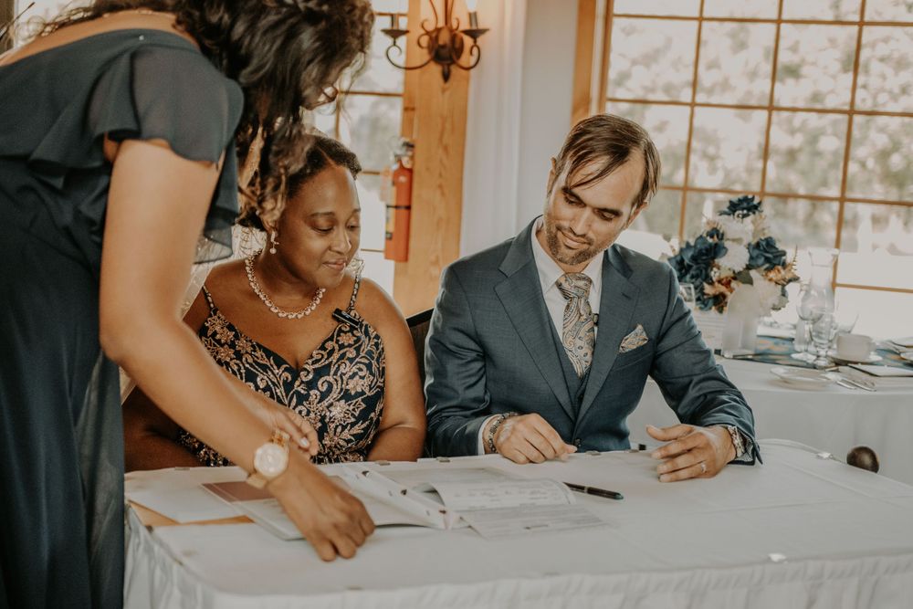Guests signing documents at a white-clothed table during a wedding ceremony.