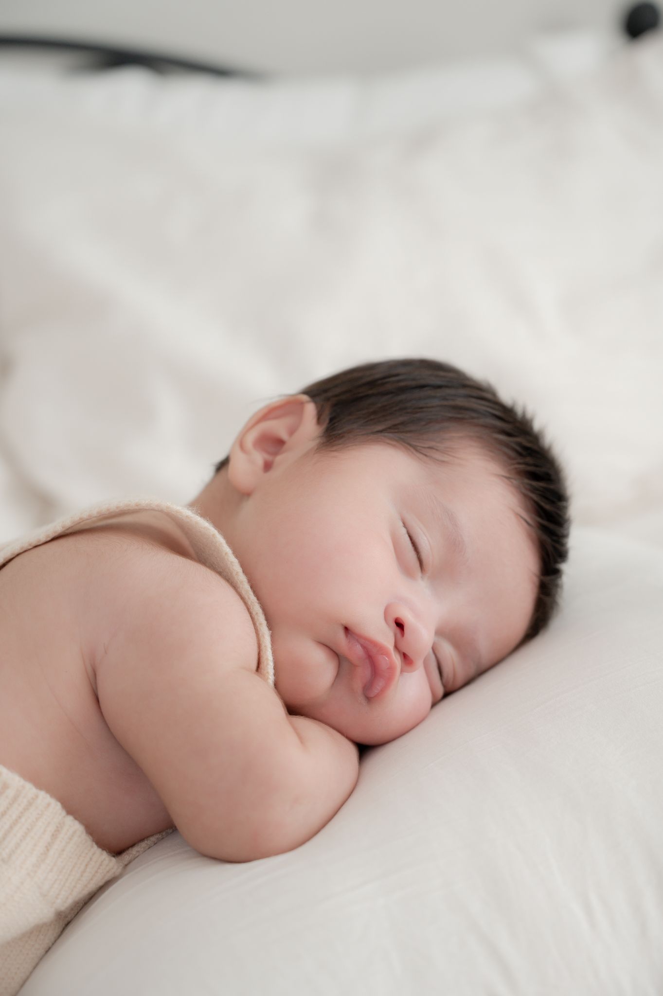 Peaceful sleeping baby wrapped in soft blankets against white bedding.