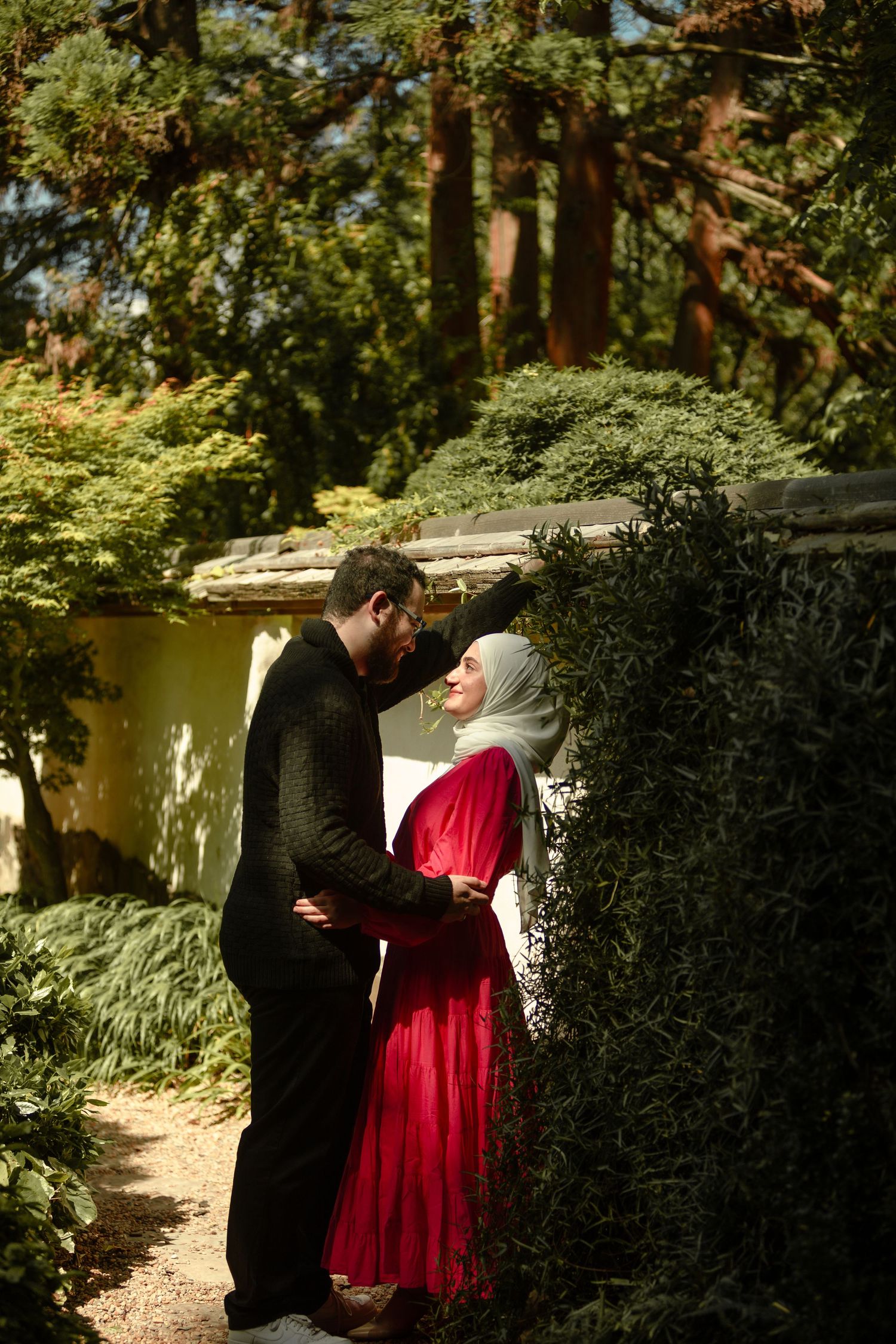 A romantic moment captured in a lush garden setting with red dress against greenery.