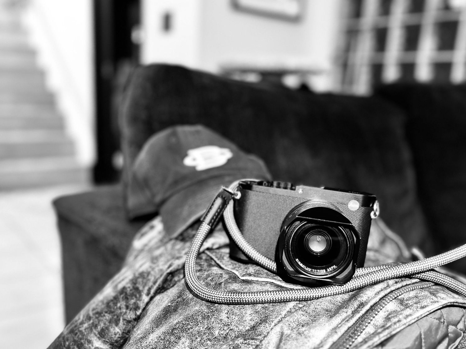 Baseball cap and digital camera sitting on dark couch in monochrome.