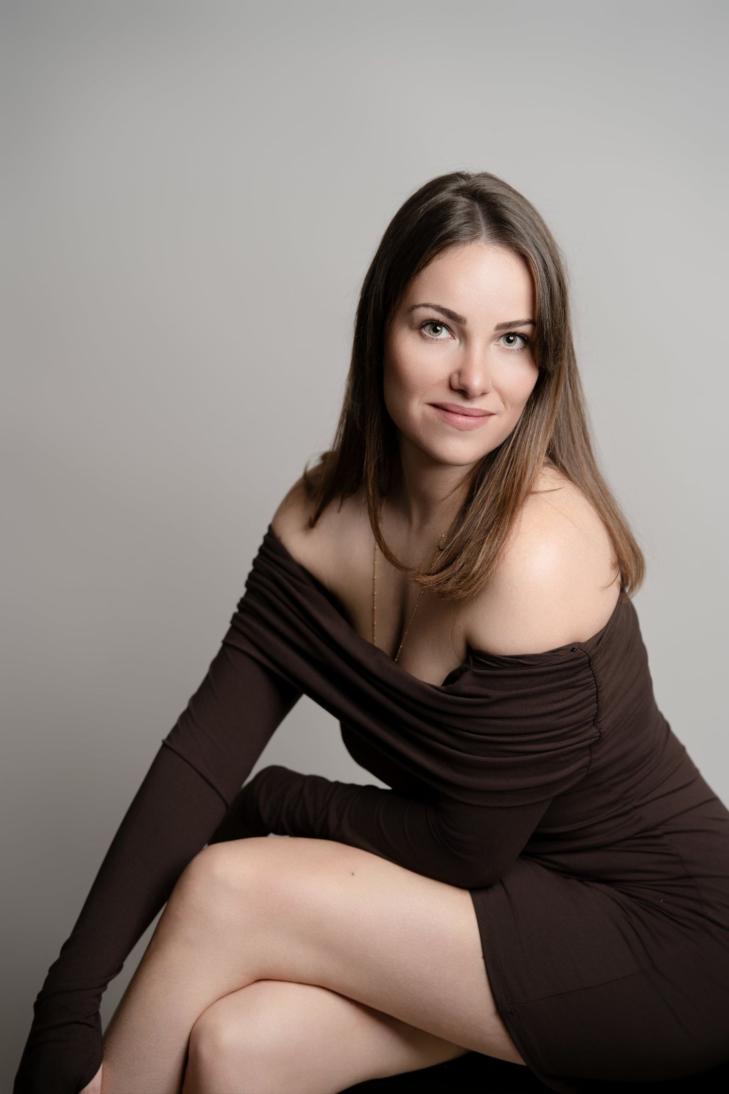 Young brunette woman in a brown off-shoulder dress posing in a professional studio portrait.