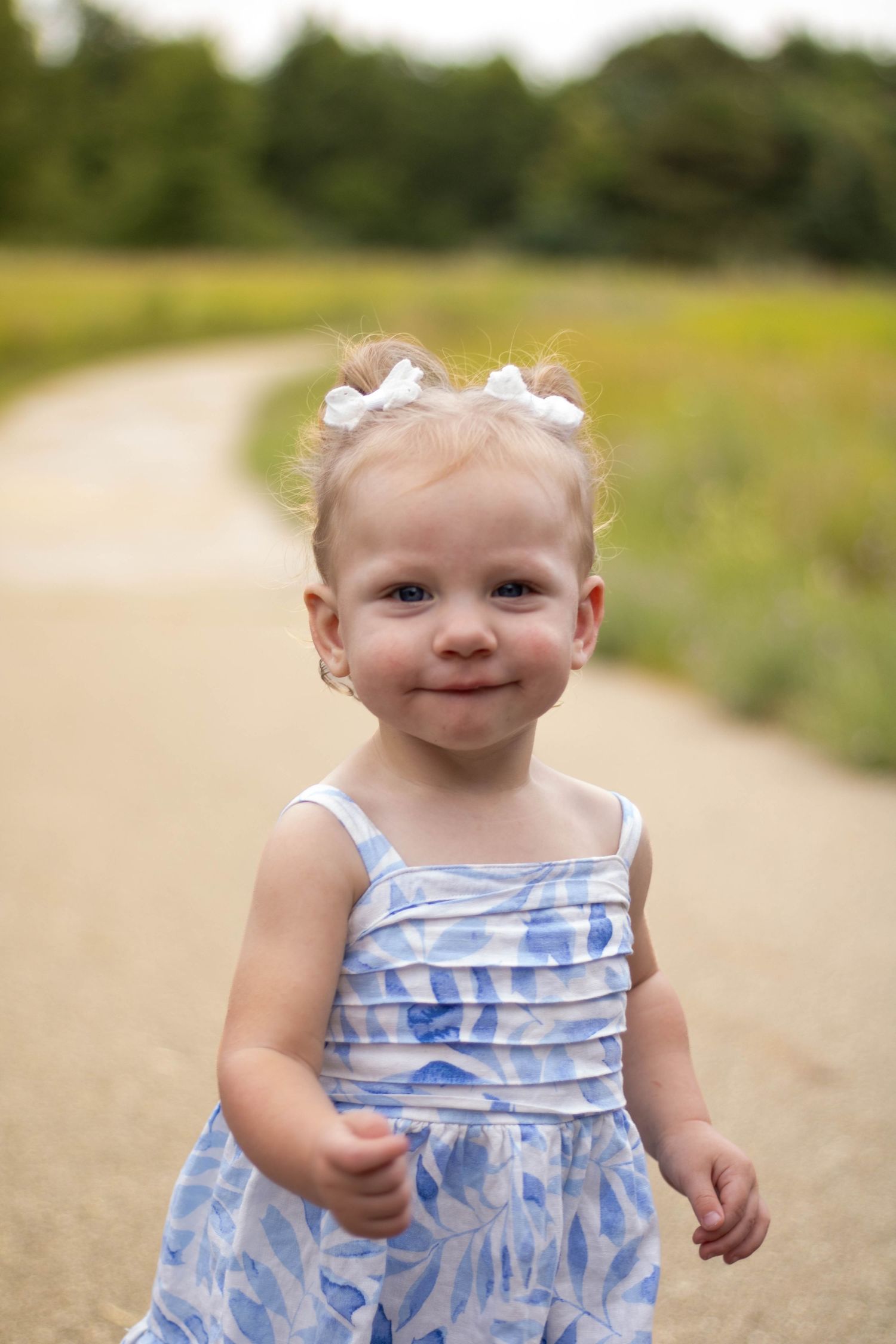 Small child wearing a blue and white patterned summer dress plays outdoors on a dirt path.