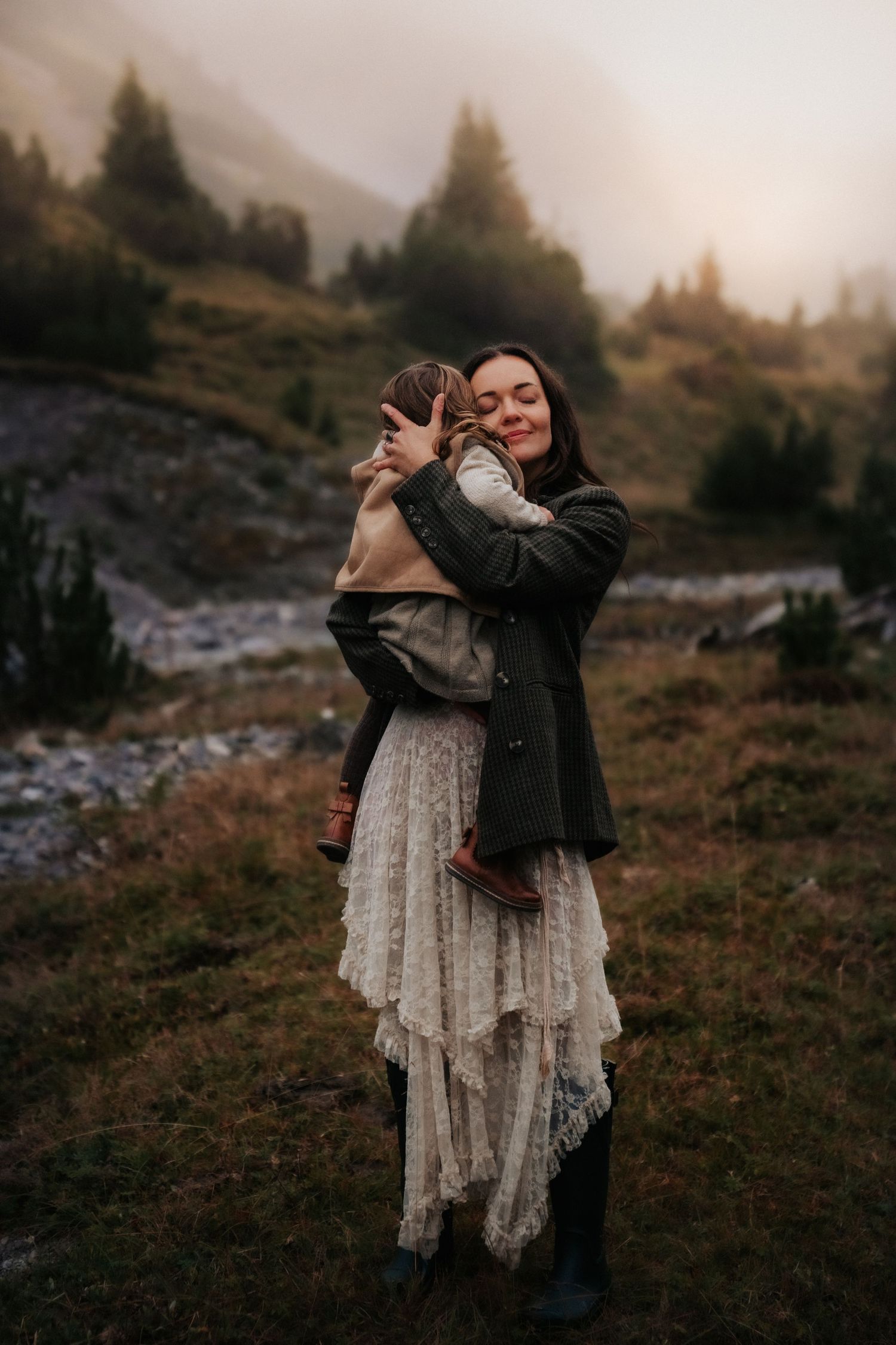 An intimate moment between parent and child against a scenic mountain backdrop at sunset.