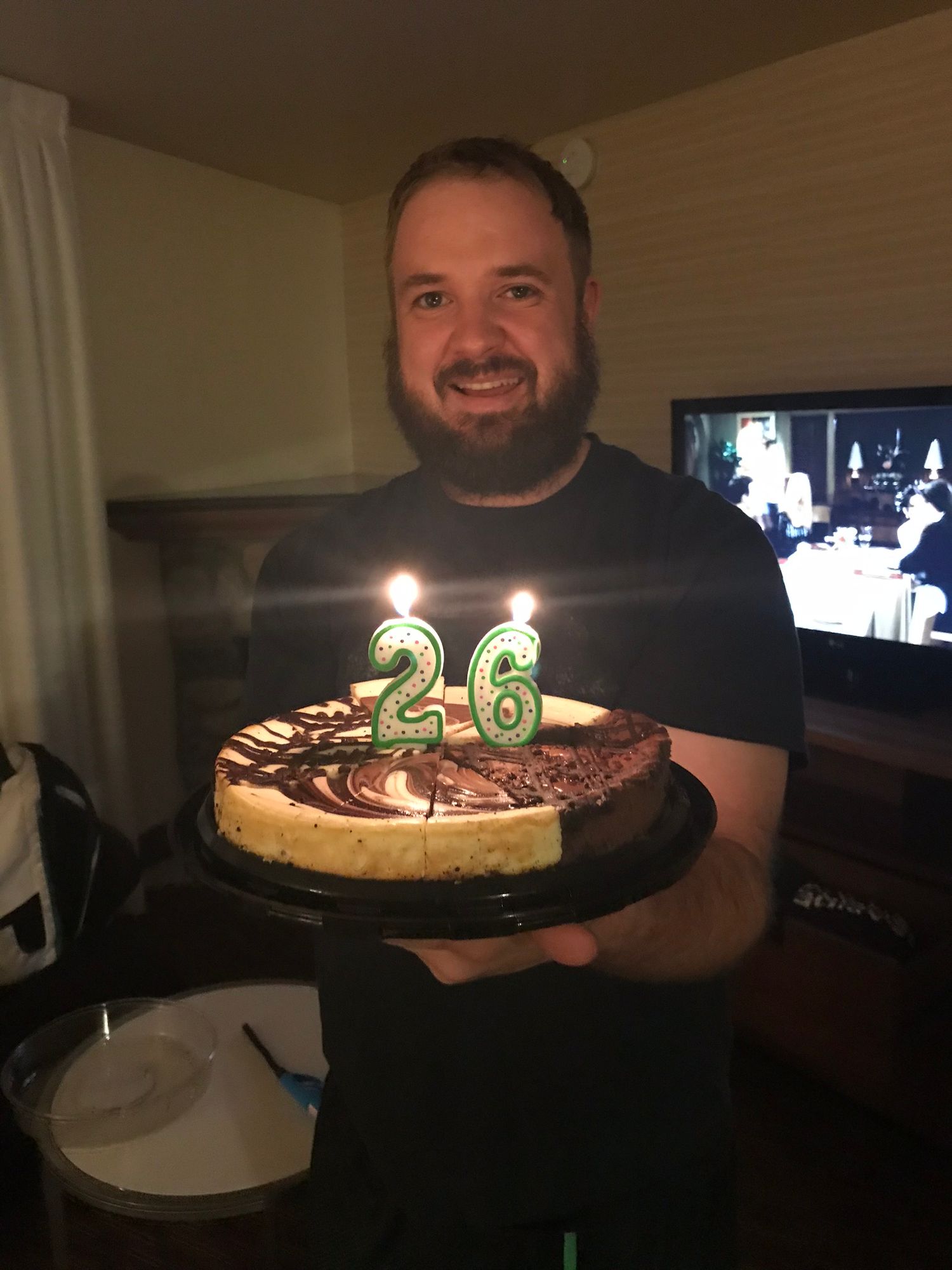 A birthday celebration with a chocolate cake displaying lit number 26 candles.