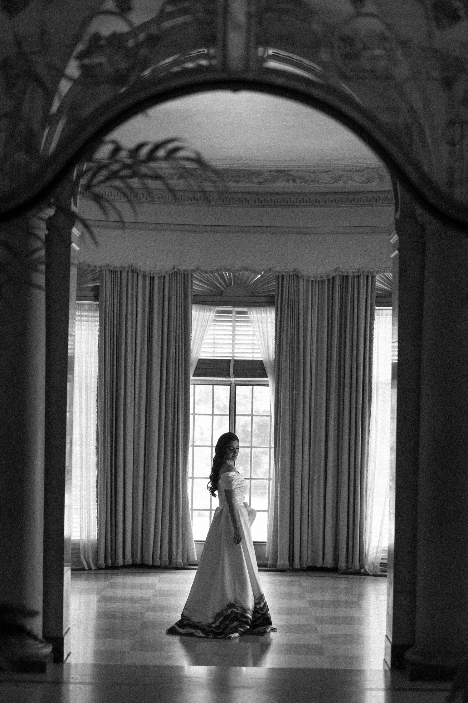 Silhouette of bride in white gown standing in elegant arched doorway.