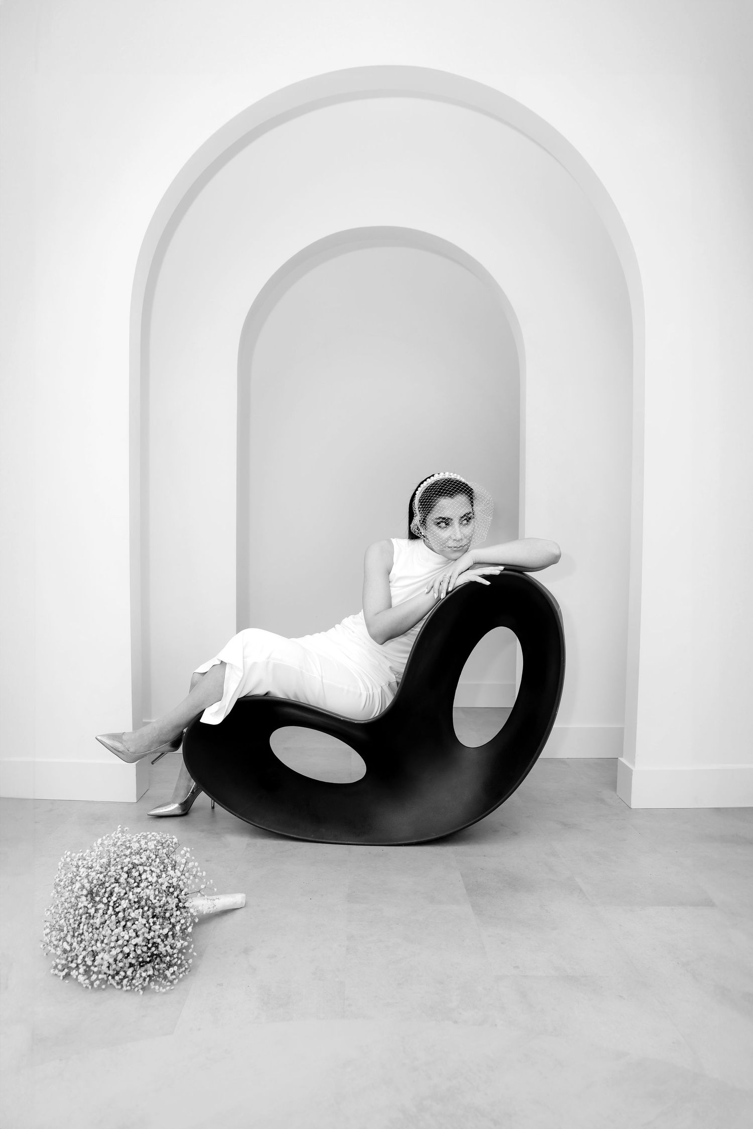 Modern bridal portrait featuring sleek white dress and dramatic curved black sculpture in minimalist arched setting.