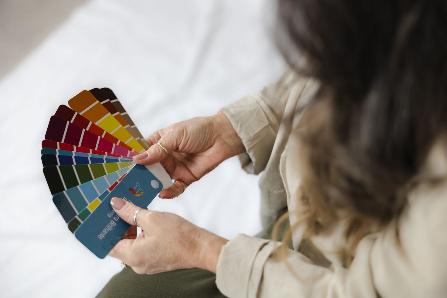 Close-up of hands holding color swatches and paint samples against white background.
