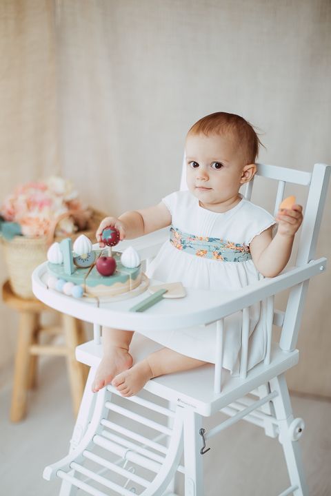 Baby sitting in white high chair playing with colorful toys and food.