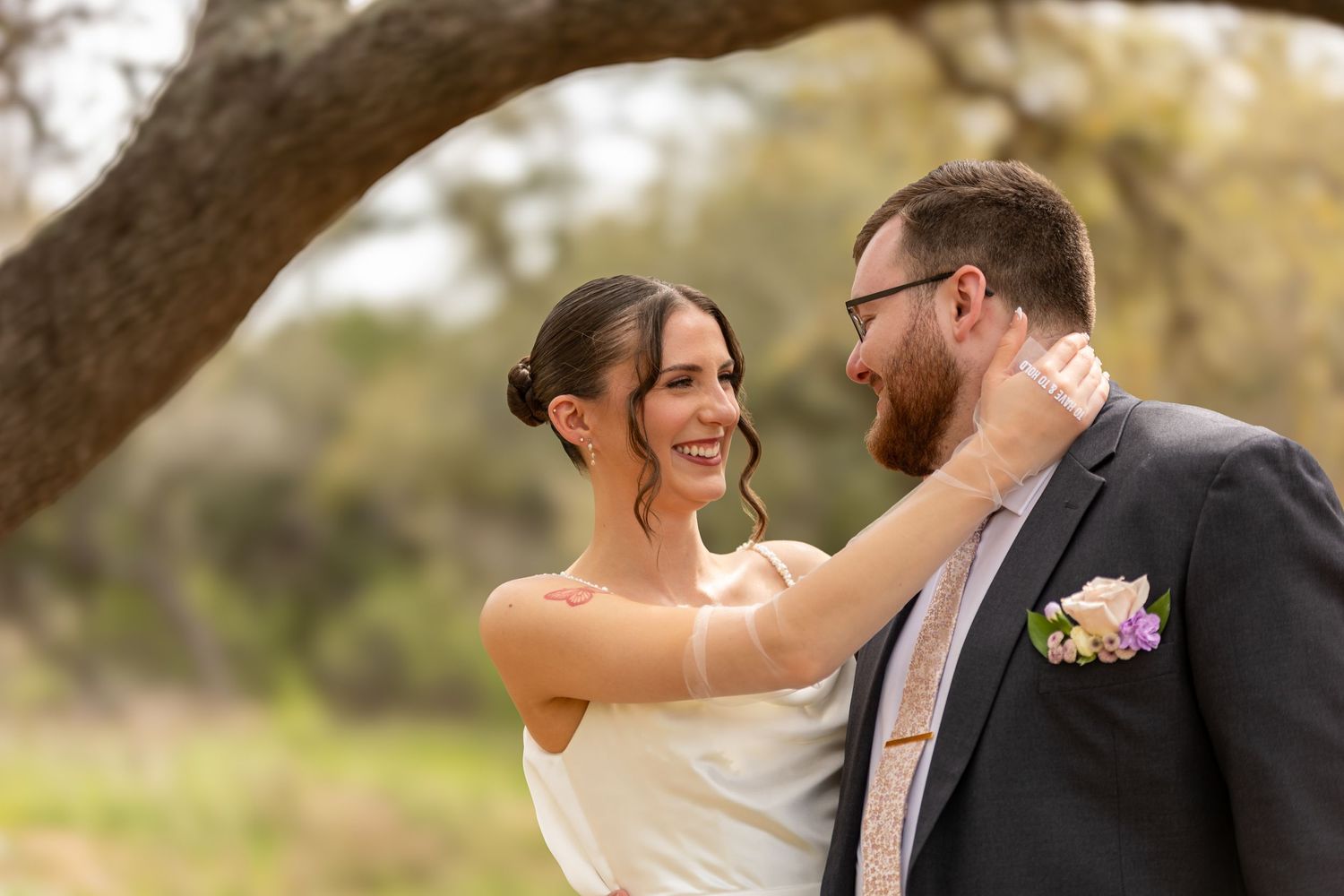 A tender moment between newlyweds outdoors as they share a loving embrace under a tree.