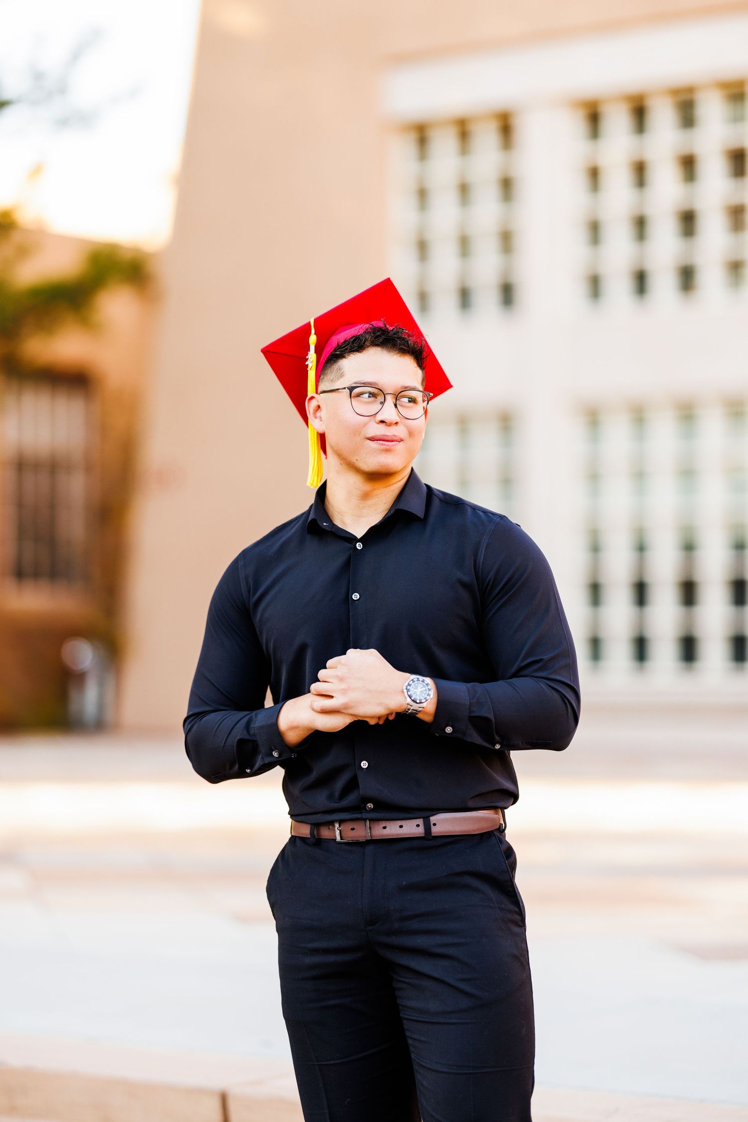 Graduation portrait with person in dark outfit and red cap against architectural background.
