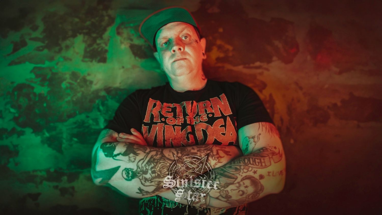 Metal musician with tattooed arms poses against dramatic red and green lighting effects.