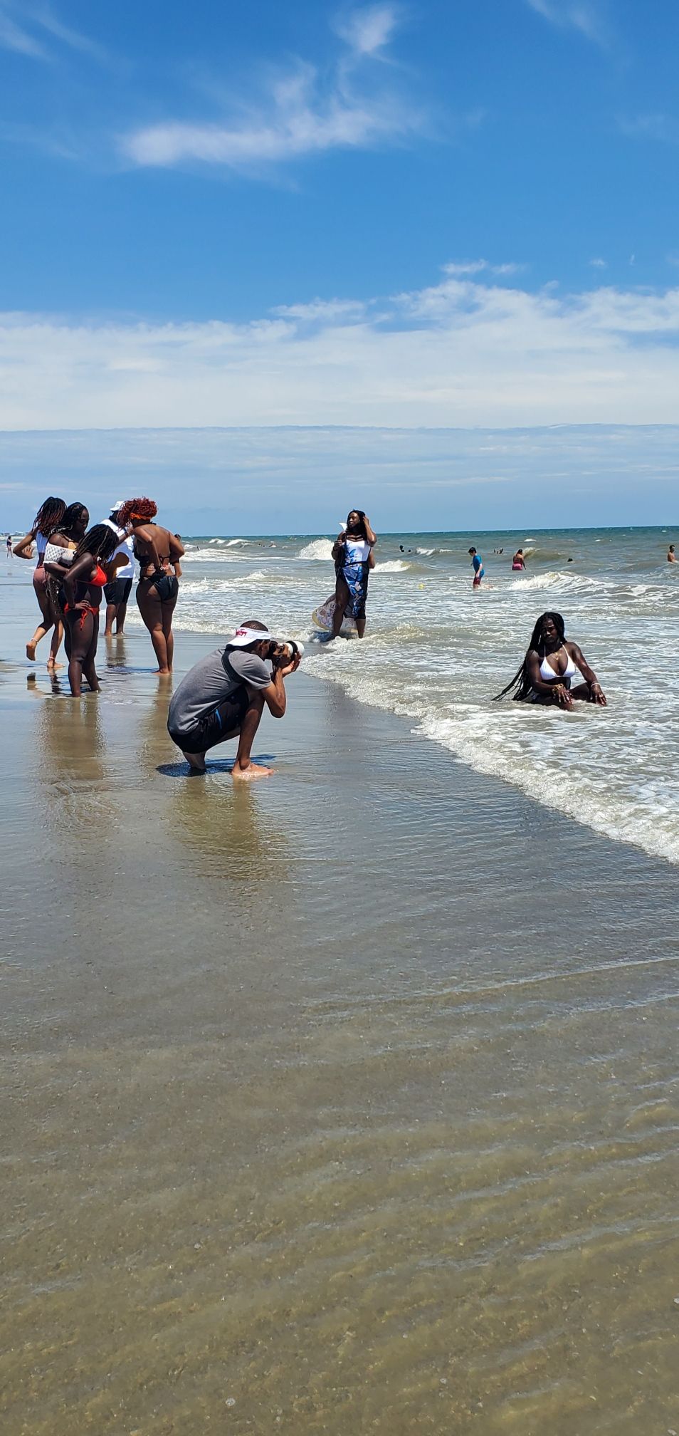 Group of photographers capturing shots at the beach shoreline on a sunny day.