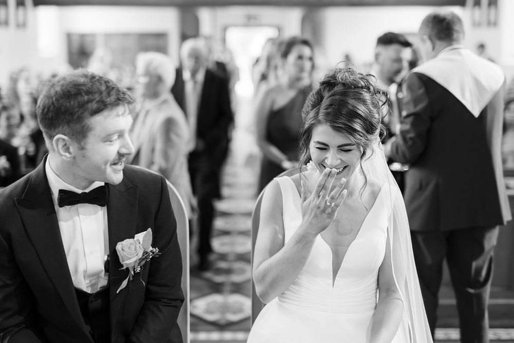 Black and white candid wedding moment captured during ceremony in county Cavan, bride giggling.