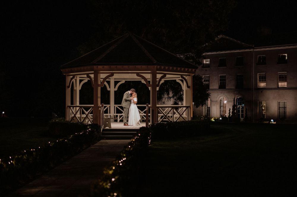 Illuminated gazebo at night with glowing pathway lights leading to a historic building in the background.