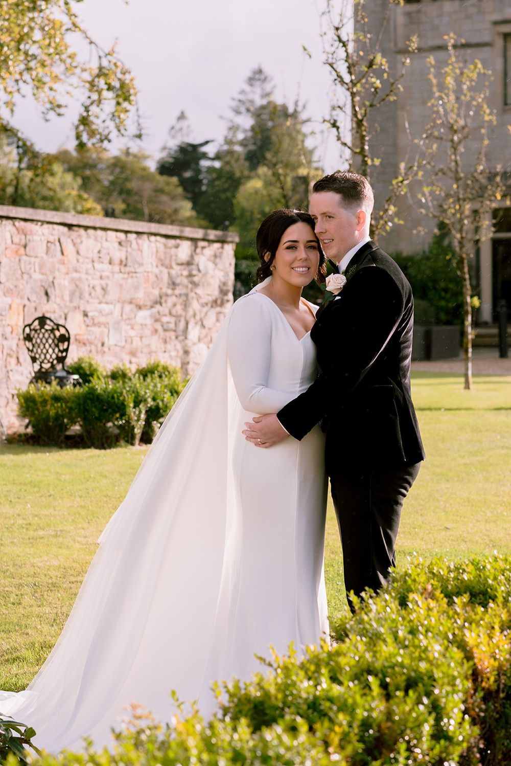 Wedding couple embracing in garden setting with stone wall backdrop in county Galway wedding venue - Lough Eske. Ireland.