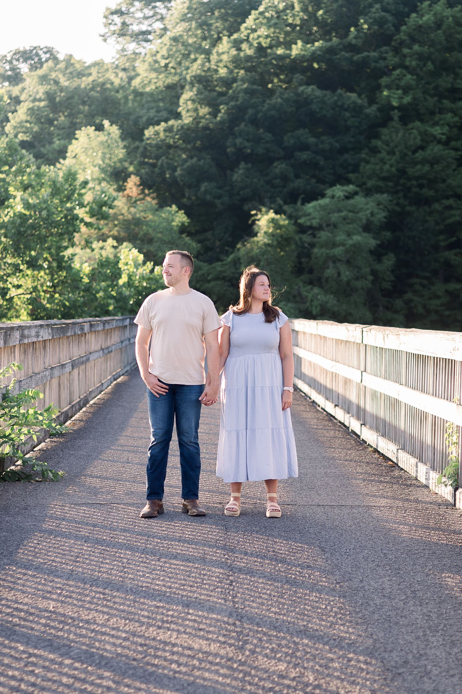 A couple walking hand in hand on a wooden bridge surrounded by lush greenery.