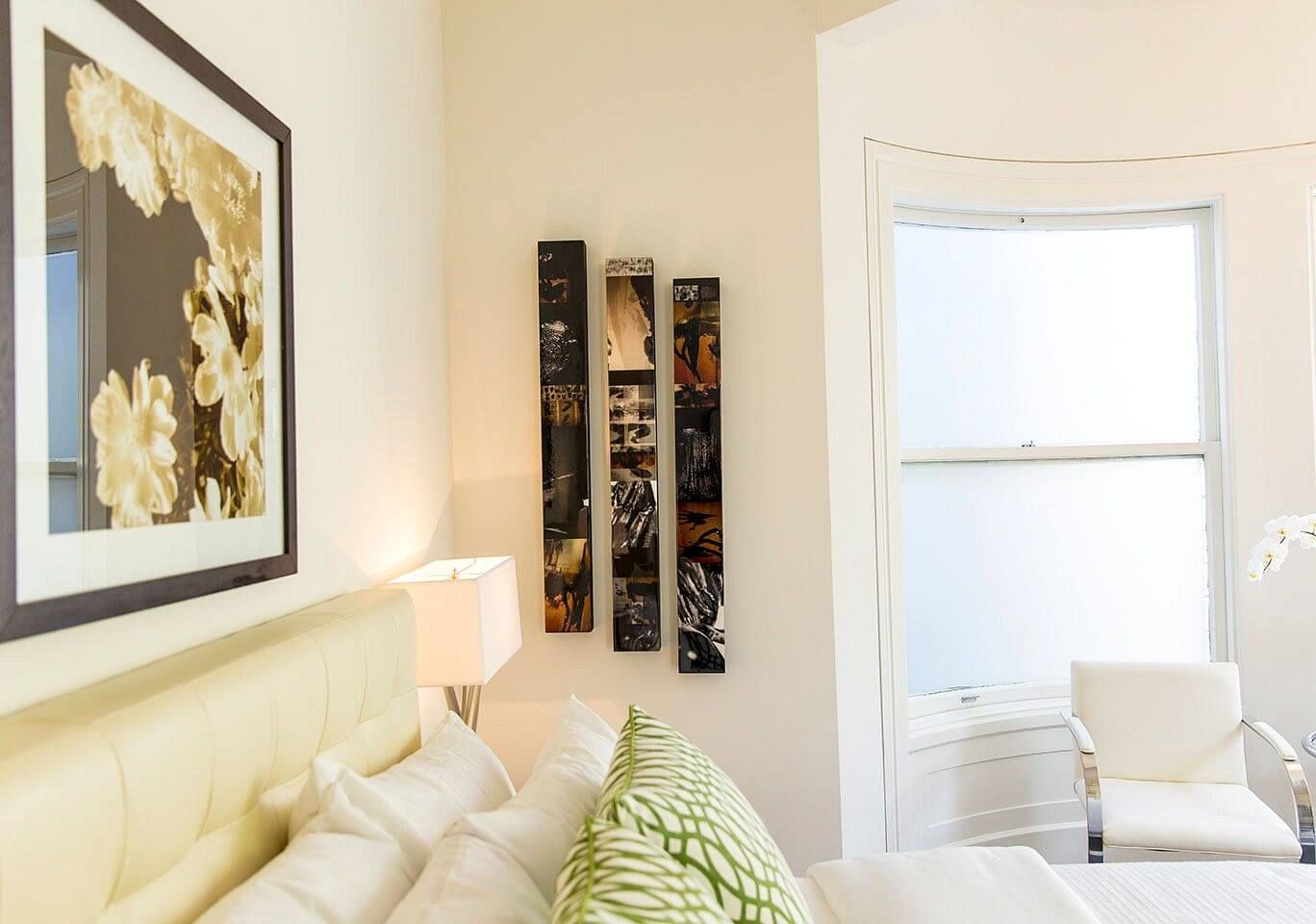 Cozy bedroom corner with floral artwork and decorative wall panels near white window.