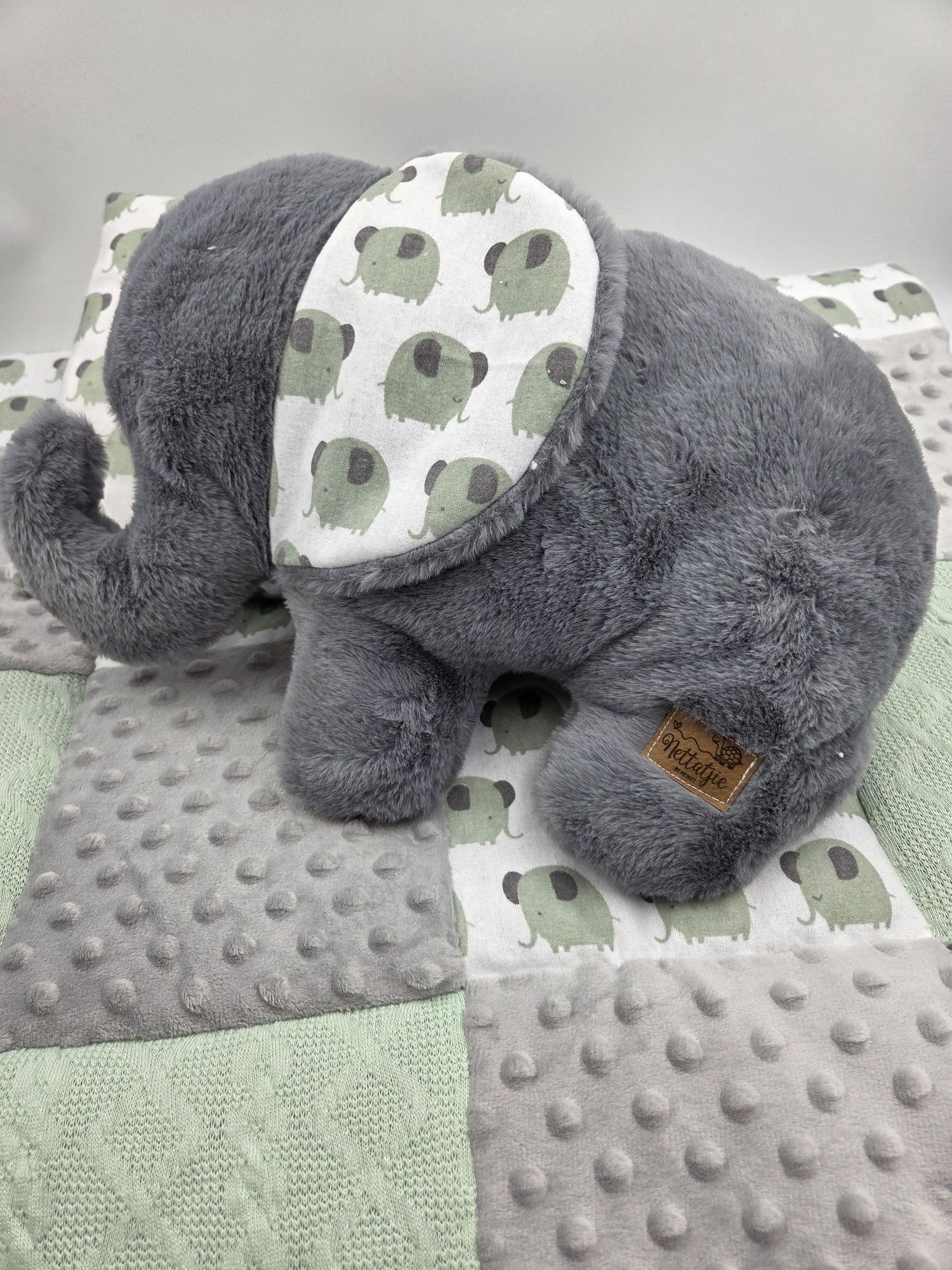 Plush gray elephant toy with patterned ears sitting on a textured minky blanket.