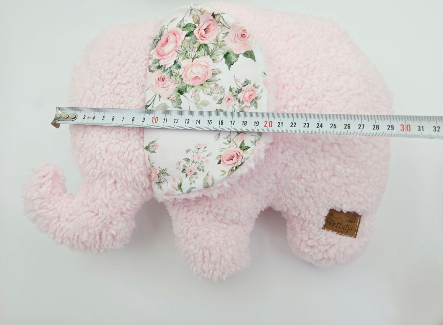 Pink plush elephant toy with floral pattern ears and measuring tape showing its size.