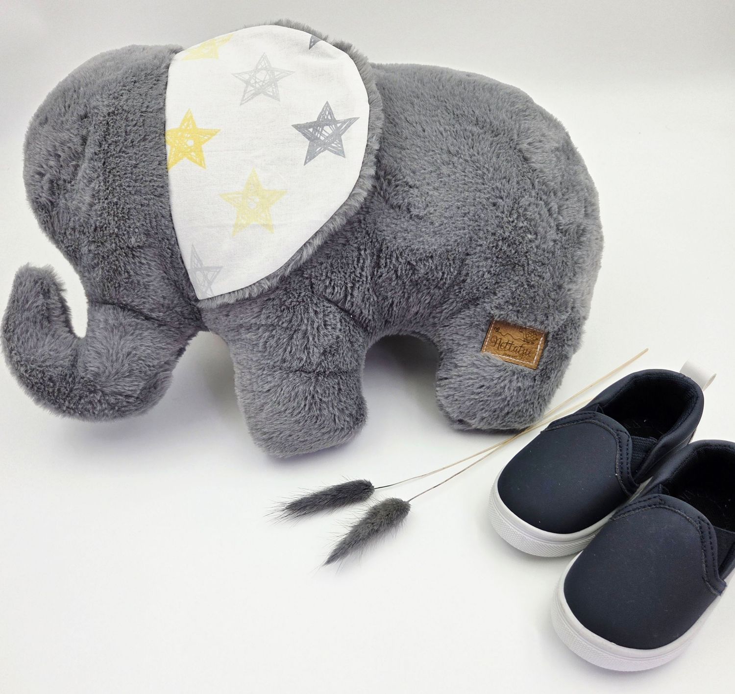 Grey plush elephant toy with star pattern ears next to navy blue shoes.