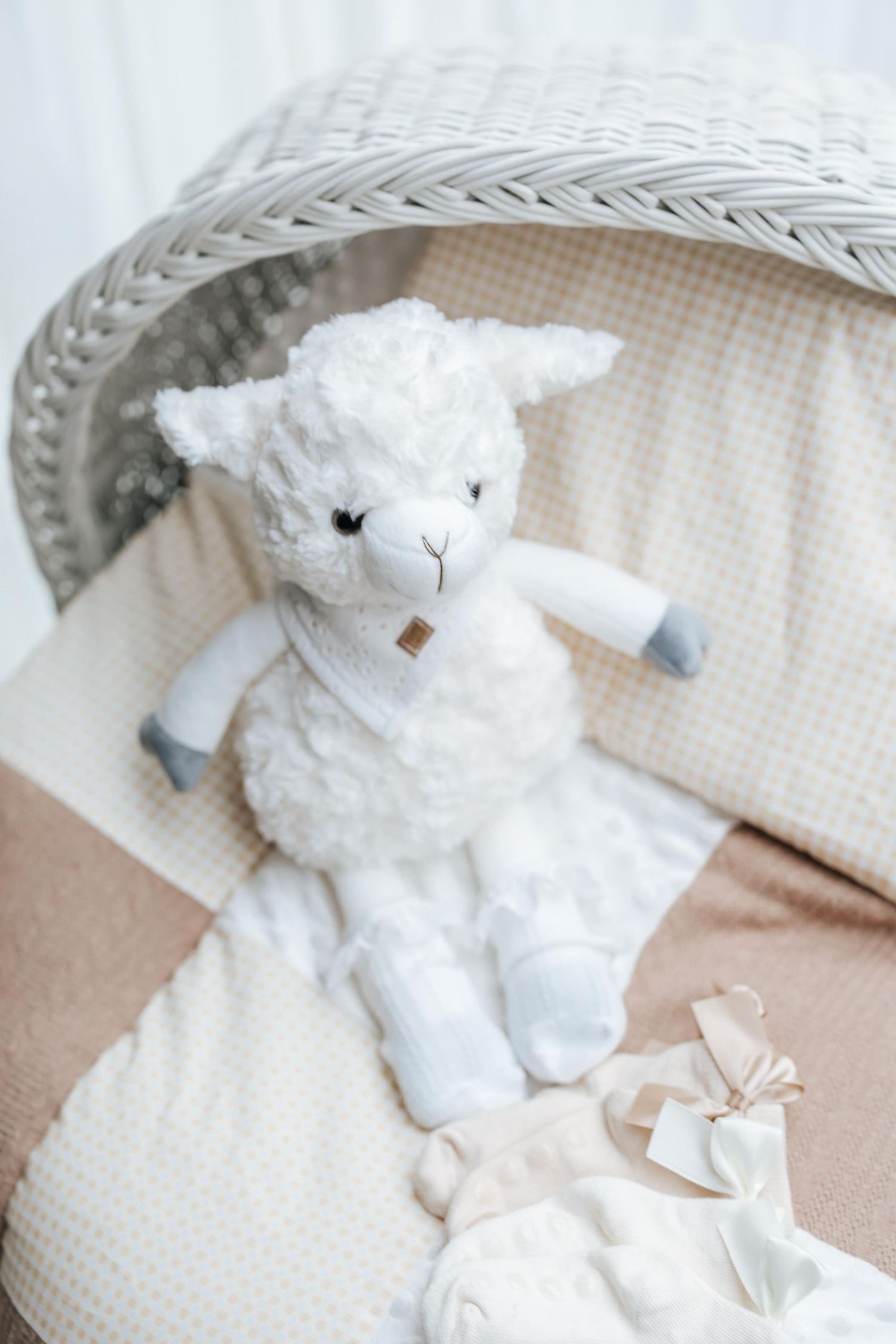 White plush lamb toy resting on textured beige blanket in wicker basket.
